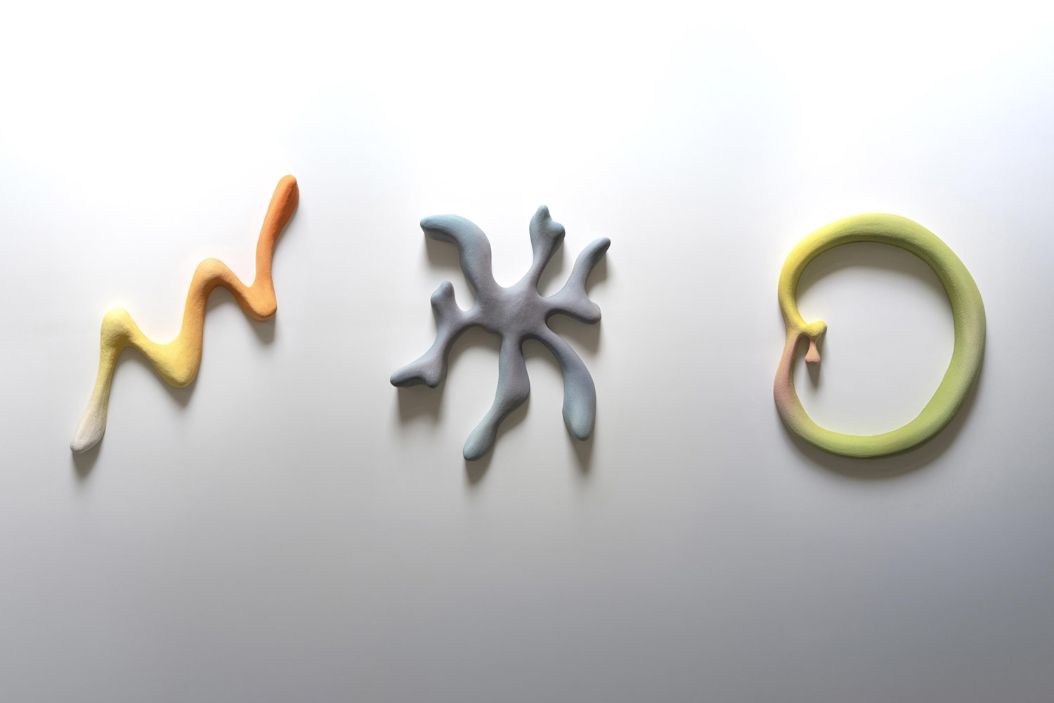 3 colourful, textured objects on a light grey background casting soft shadows below: the first object resembles an abstract lighting bolt with a gradient from white to orange, the second object has an amorphous shapes with 7 arms and colours ranging from light blue to soft purple, the third object with a circular ring shape with a dent on left with a seed-like element and colours ranging from light pink to bright yellow to light green